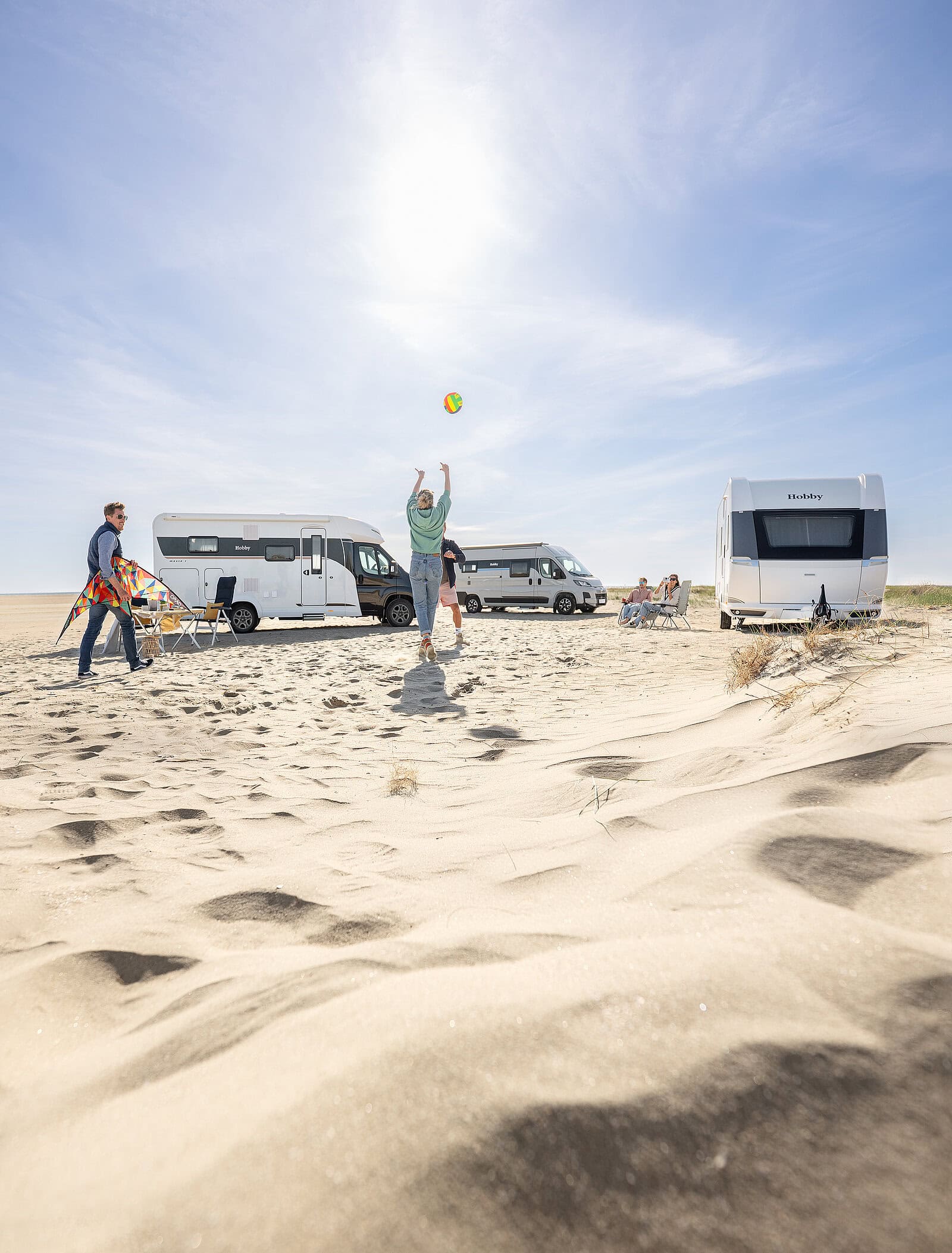 Familj leker med boll utanför en Husbil, husvagn och campervan på en solig strand